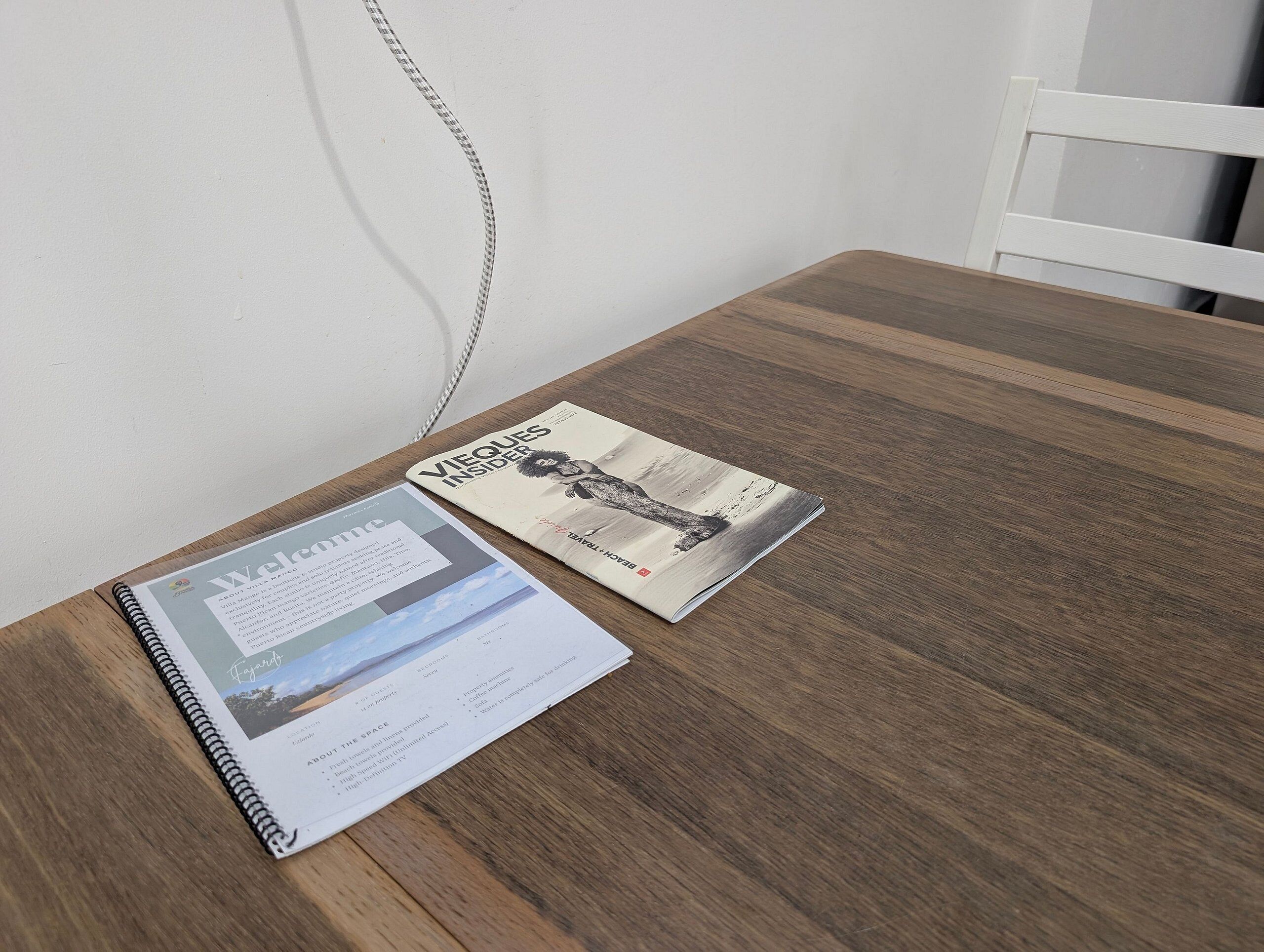 Un petit livre à spirale, posé sur une table en bois, à côté d’un magazine dont la couverture représente une personne et un paysage.
