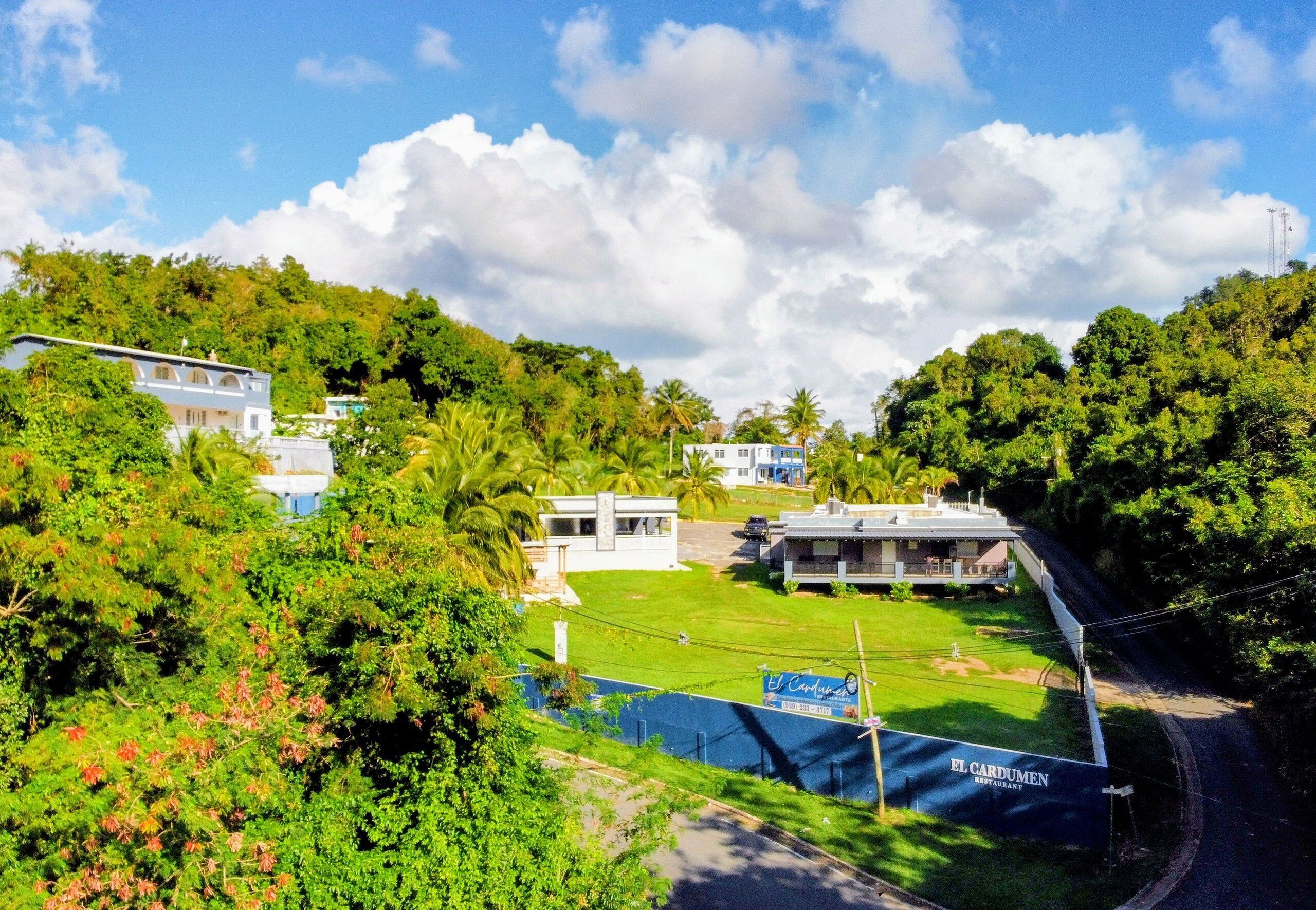 A hotel with a view of a lush green landscape, a swimming pool, and a sign for El Cardumen Restaurant.