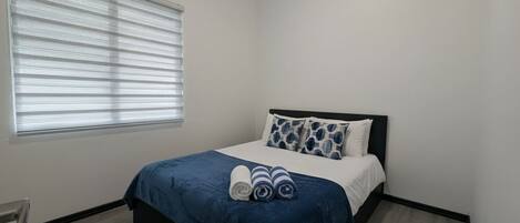 A bedroom with a bed, a window with blinds, a chair, and a wall-mounted air conditioner.