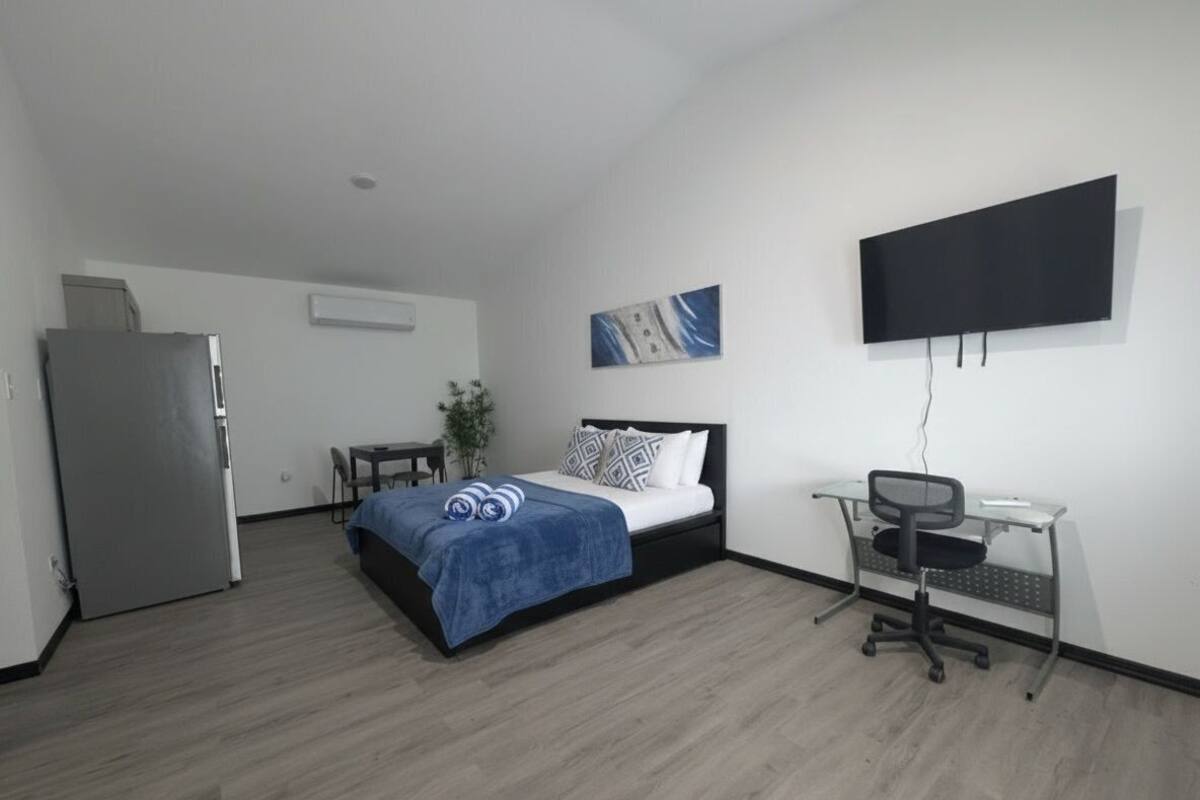A modern hotel room with a bed, desk, chair, flat-screen TV, and a small table.
