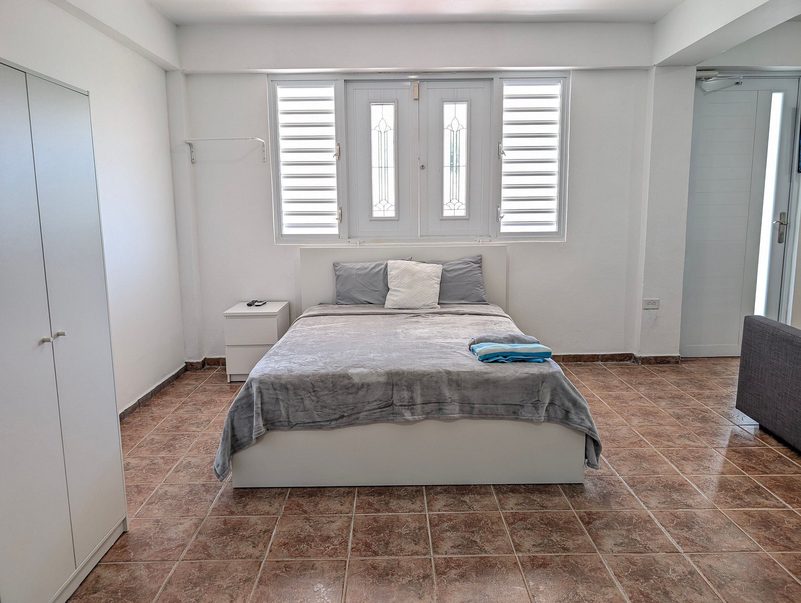 A bedroom with a bed, a nightstand, a wardrobe, and a window with blinds.