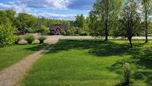 Ett lantligt landskap med en grusväg, grönt gräs, träd och en röd byggnad.