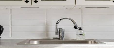 Una cocina con armarios blancos, un lavamanos de acero inoxidable y un grifo.
