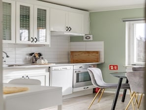 A modern kitchen with white cabinets, a wooden countertop, and a dining area with a grey chair. - Charming 2-bedroom Apartment in Rejmyre With Garden View (Rejmyre)
