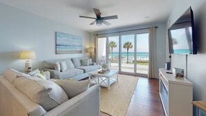 Un salon avec un canapé, une table basse et un téléviseur, donnant sur une plage.