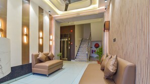 A hotel lobby with a reception desk, two sofas, a staircase, and a potted plant. - Hotel Starlink By The Nine Hotel  (Jaipur)