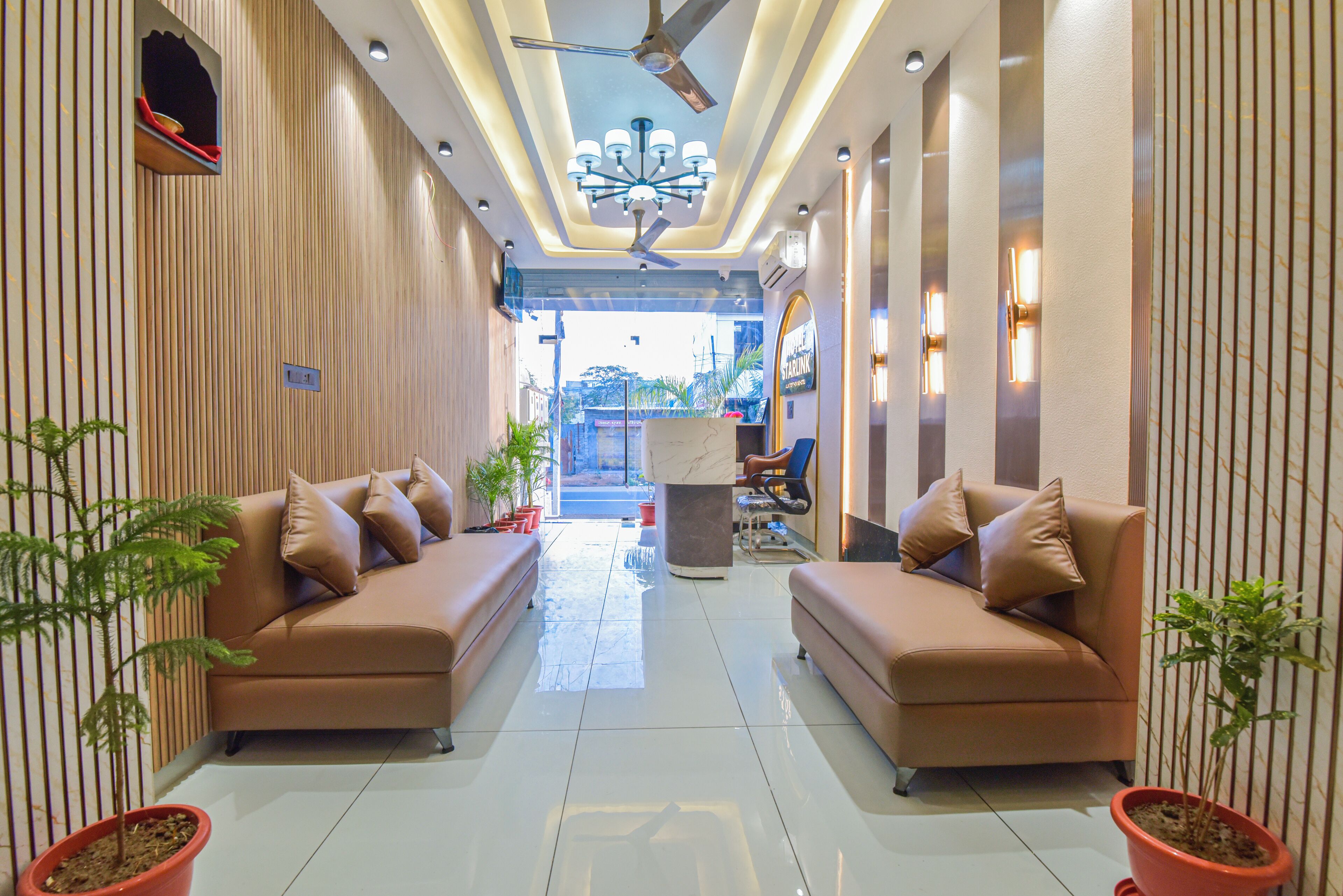 A modern lobby with two sofas, potted plants, a ceiling fan, and a view of the outside.
