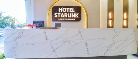 A márvány munkalappal ellátott szállodai recepció, amelyen egy tábla jelzi: „HOTEL STARLINK – A NINE HOTEL EGYEGYSÉGE”.