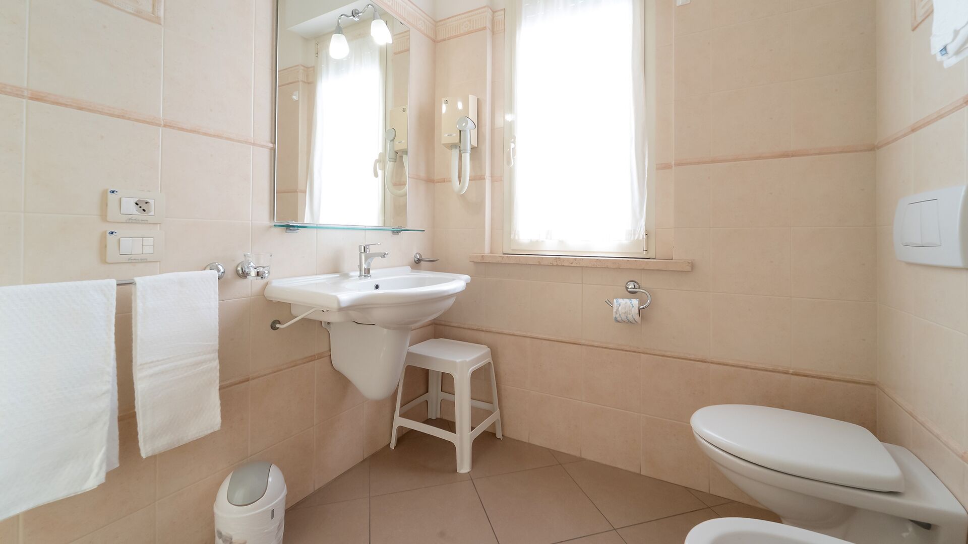 Un baño con lavamanos, espejo, inodoro y un taburete pequeño.