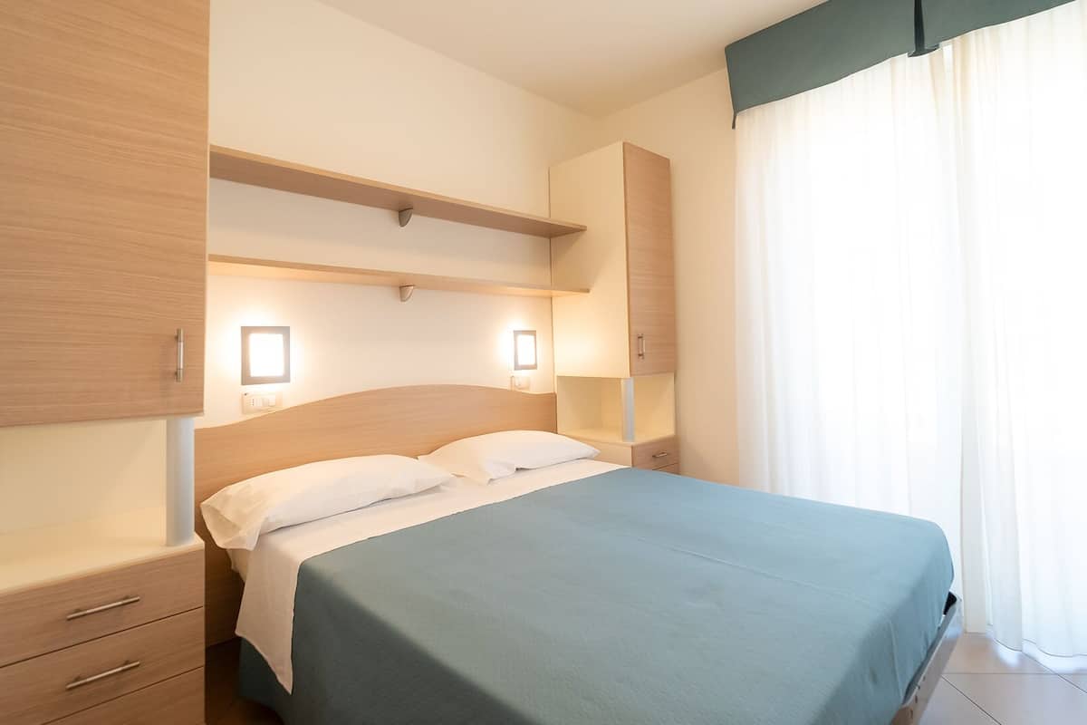 Hotellihuone, jossa on sänky, yöpöydät, vaatekaappi ja pieni sivupöytä.
