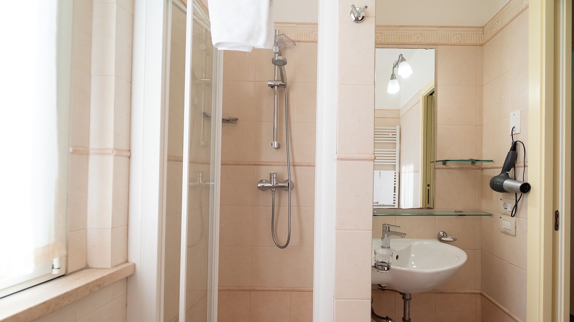 Een badkamer met een glazen douchecabine, een wit wastafeltje en een spiegel.
