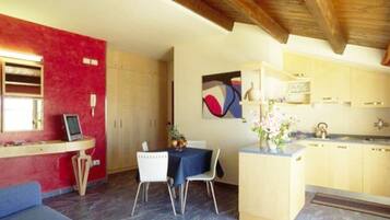 A compact kitchen with a dining area, featuring a red wall, wooden cabinets, and a painting.