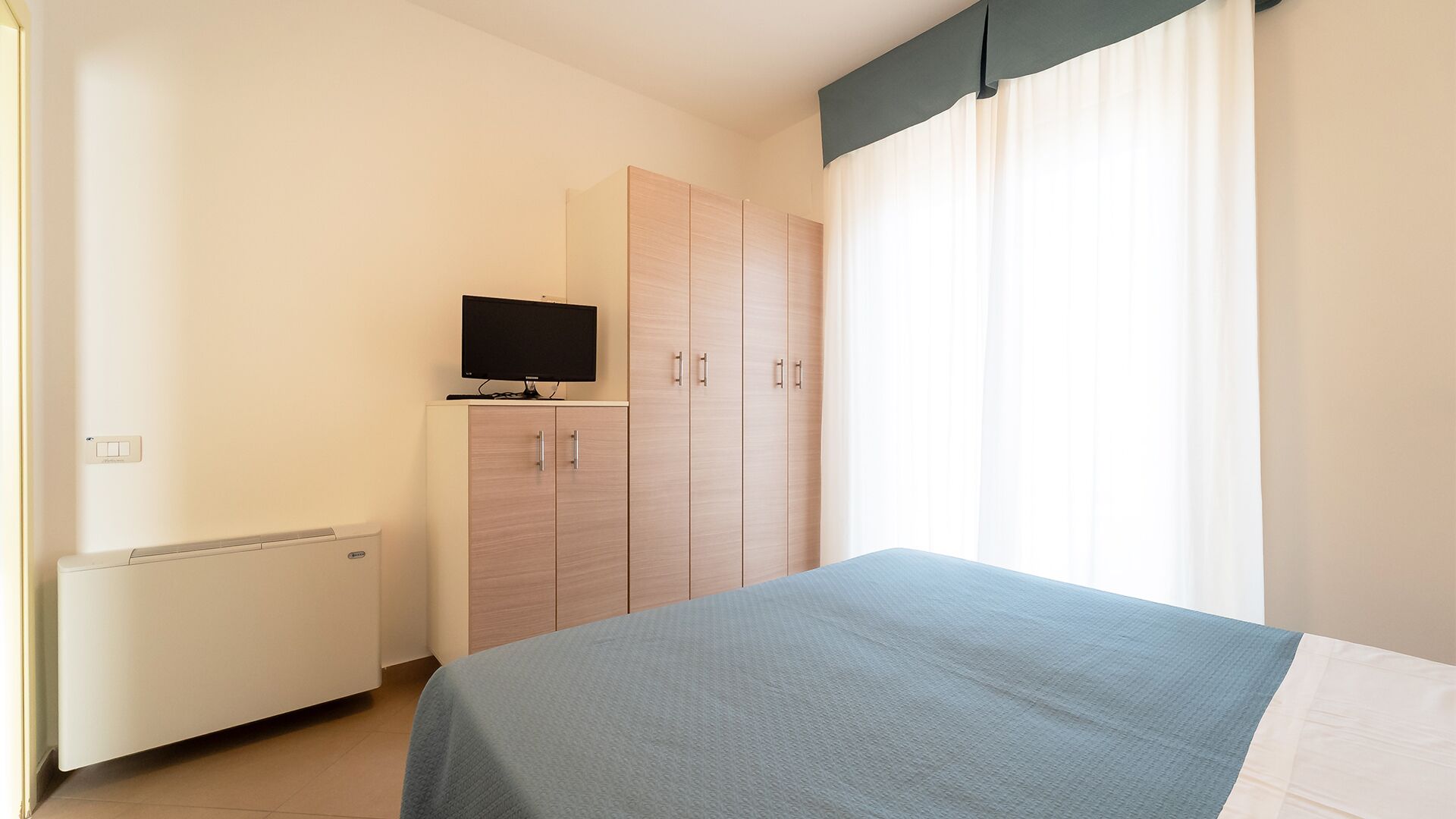 A bedroom with a bed, a wardrobe, a television, and a radiator.