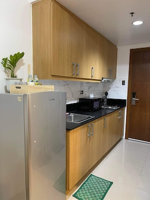 Eine moderne Küche mit Holzausstattung, einem Edelstahlkühlschrank, einer schwarzen Mikrowelle und einem Spülbecken.