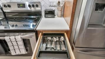 A kitchen with a stove, toaster, and a drawer with utensils.
