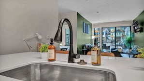 A modern kitchen with a stainless steel sink, two bottles of soap, a white lamp, and a view of the outside through large windows.