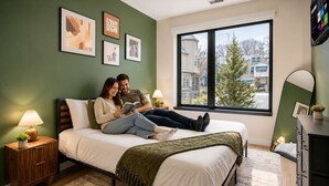 A bedroom with a bed, bedside lamps, a dresser, a window with a view, and framed artwork on the wall.