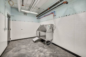 A clean, industrial-style room with white tiled walls, a stainless steel machine, and visible plumbing and electrical conduits.