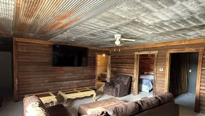 Ein rustikales Holzhütten-Interieur mit einem braunen Ledersofa, einem Liegesessel und einem an der Wand befestigten Fernseher.