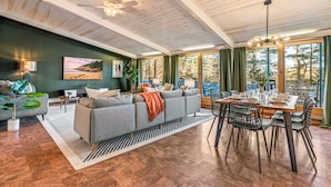 A spacious living room with a large gray sectional sofa, a dining table with chairs, and a ceiling fan. - Acadia Home with Hot Tub and Game Room (Mount Desert)