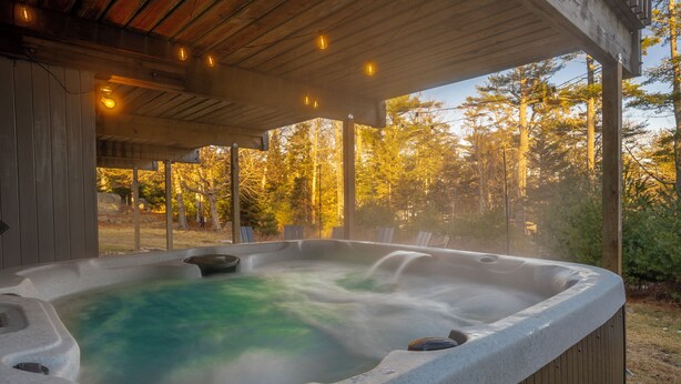 A hot tub with a wooden deck and a view of trees. - Acadia Home with Hot Tub and Game Room (Mount Desert)