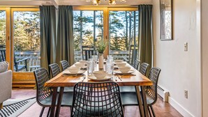 A dining area with a wooden table set for six, surrounded by chairs with a grid pattern. - Acadia Home with Hot Tub and Game Room (Mount Desert)