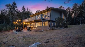 A two-story house with a balcony, surrounded by trees. - Acadia Home with Hot Tub and Game Room (Mount Desert)