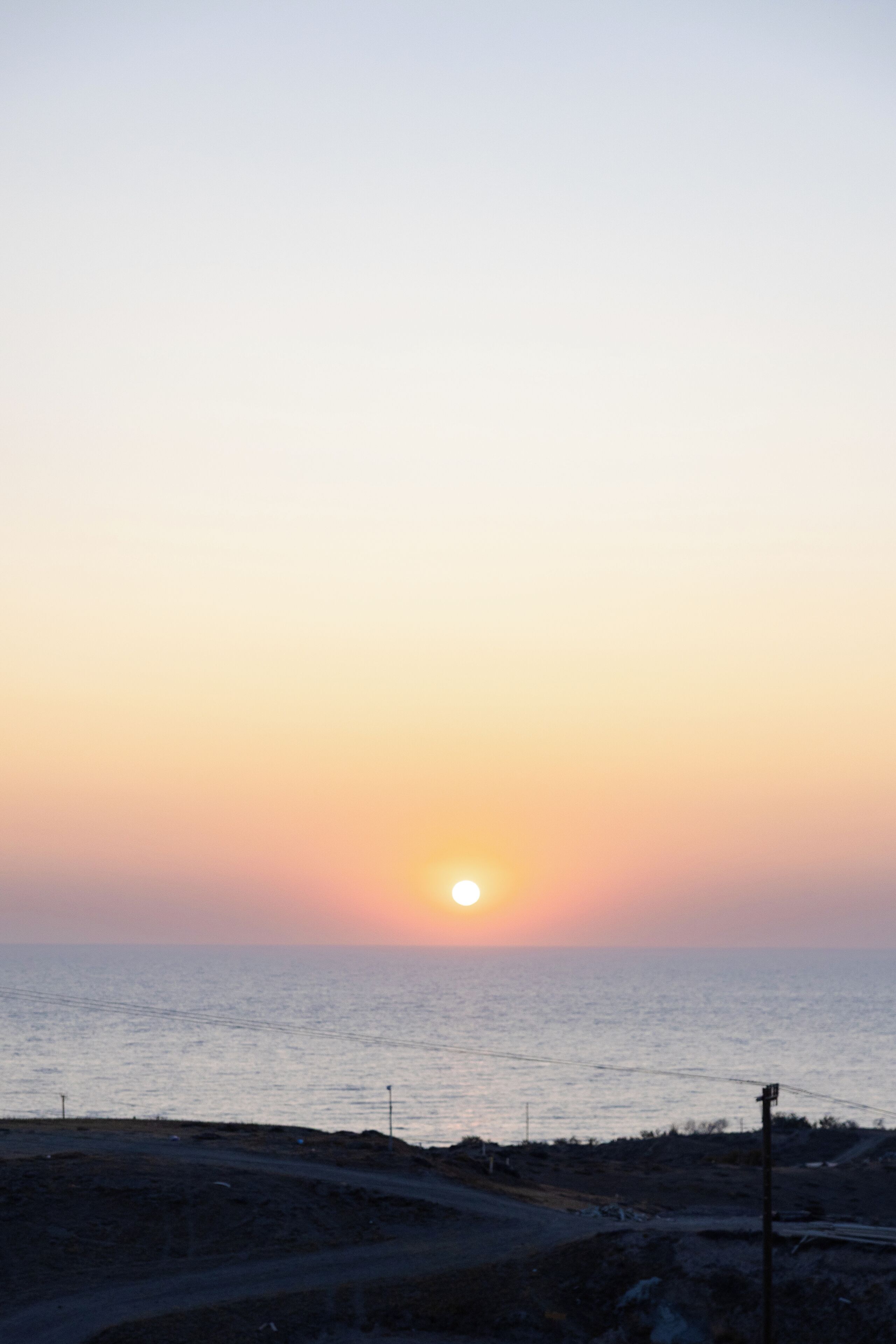 A sunset over a coastal area with a road and utility poles.