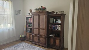 Habitació amb una gran estanteria de fusta plena de llibres, una cistella de vímet i una petita planta en test.