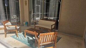 Un pati enllumenat pel sol, amb mobles de fusta, incloent un sofà i cadires, i una taula petita.