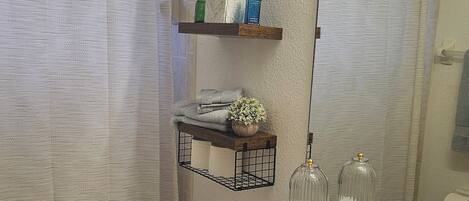 A bathroom with a toilet, sink, and a mirror. There are shelves with toiletries and a potted plant.
