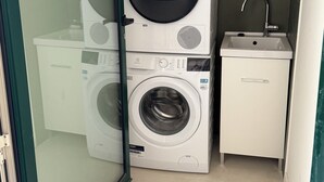 Ein kleiner Waschraum mit zwei übereinander gestapelten Waschmaschinen, einem Waschbecken und einem kleinen Schrank.