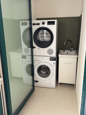 Ein kleiner Waschraum mit zwei übereinander gestapelten Waschmaschinen, einem Waschbecken und einem kleinen Schrank.