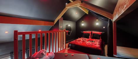 A bedroom with a red bed, a wooden ceiling, and a red railing.