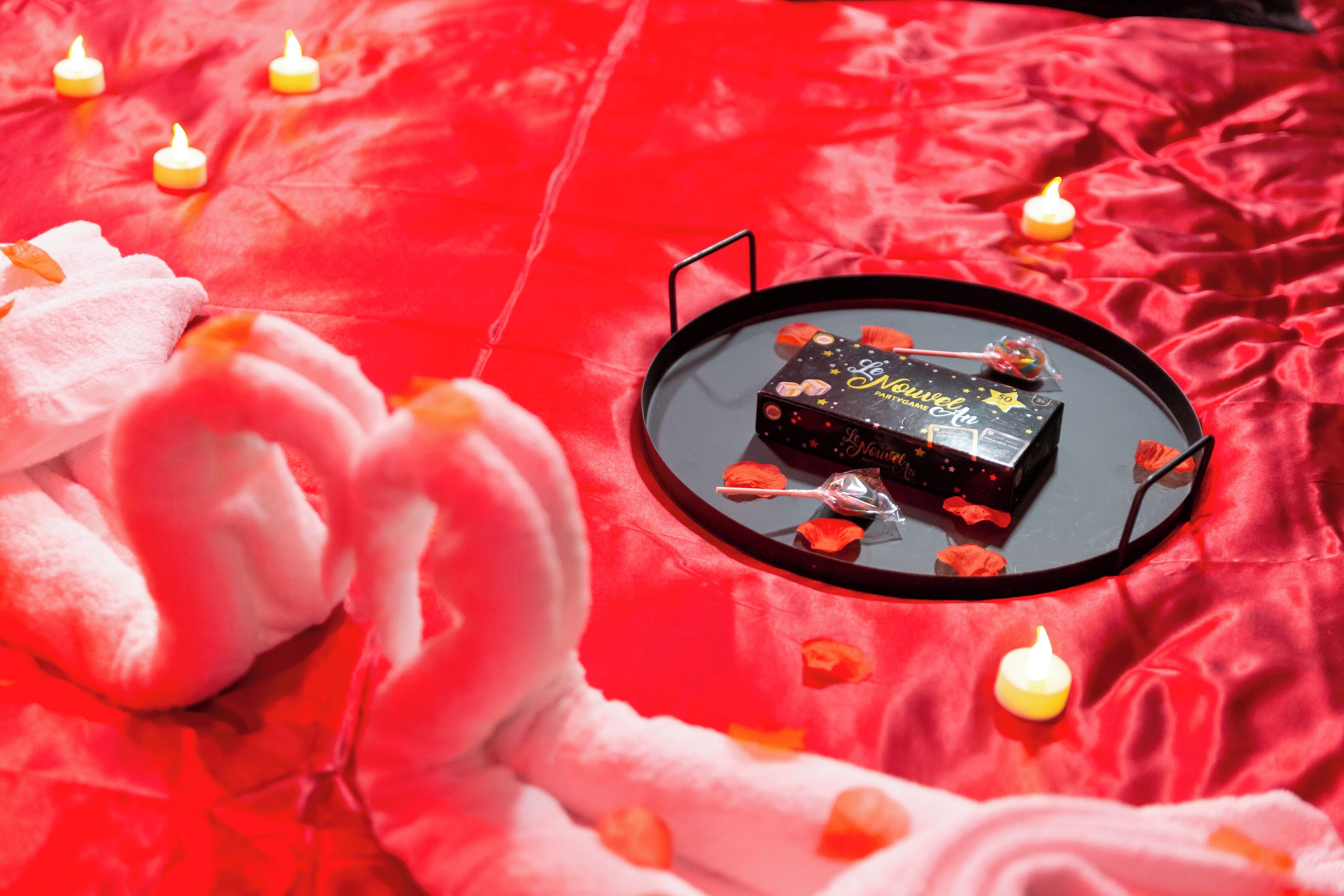 A bed with a red satin cover, a black tray with a chocolate bar, and scattered rose petals.