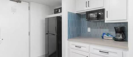 A compact kitchen with white cabinets, a black refrigerator, a microwave, and a coffee maker on the countertop.