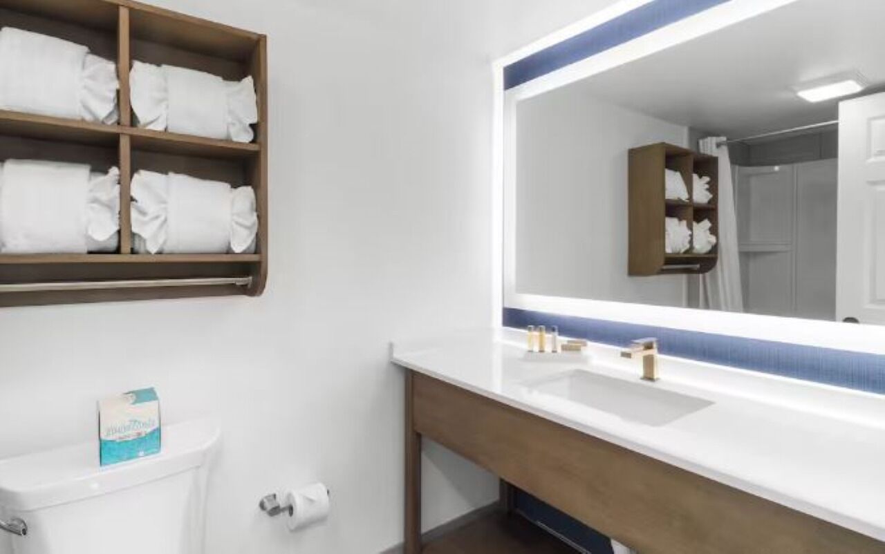 Une salle de bain avec un lavabo blanc, un miroir à cadre bleu et une étagère en bois où sont pliées des serviettes.