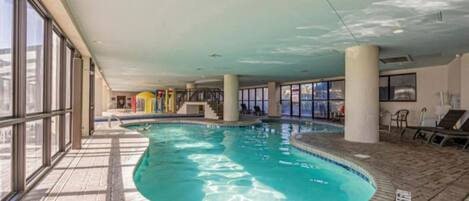 An indoor swimming pool with clear water, tiled flooring, and large windows on one side.