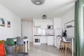 A modern kitchen with white cabinets, a dining area with a table and chairs, and a bar area with stools.