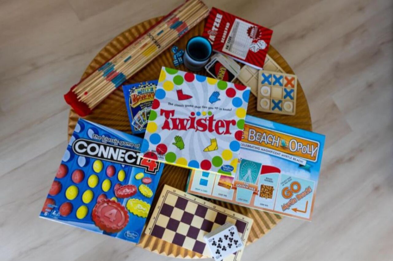 Diversos jocs de taula, com Twister, Connect 4 i Monopoly, disposats sobre una taula de fusta rodona.