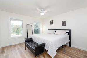 A bedroom with a bed, a bench, two windows, and a ceiling fan.