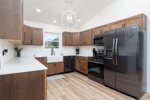 A modern kitchen with wooden cabinets, stainless steel appliances, and a geometric pendant light.