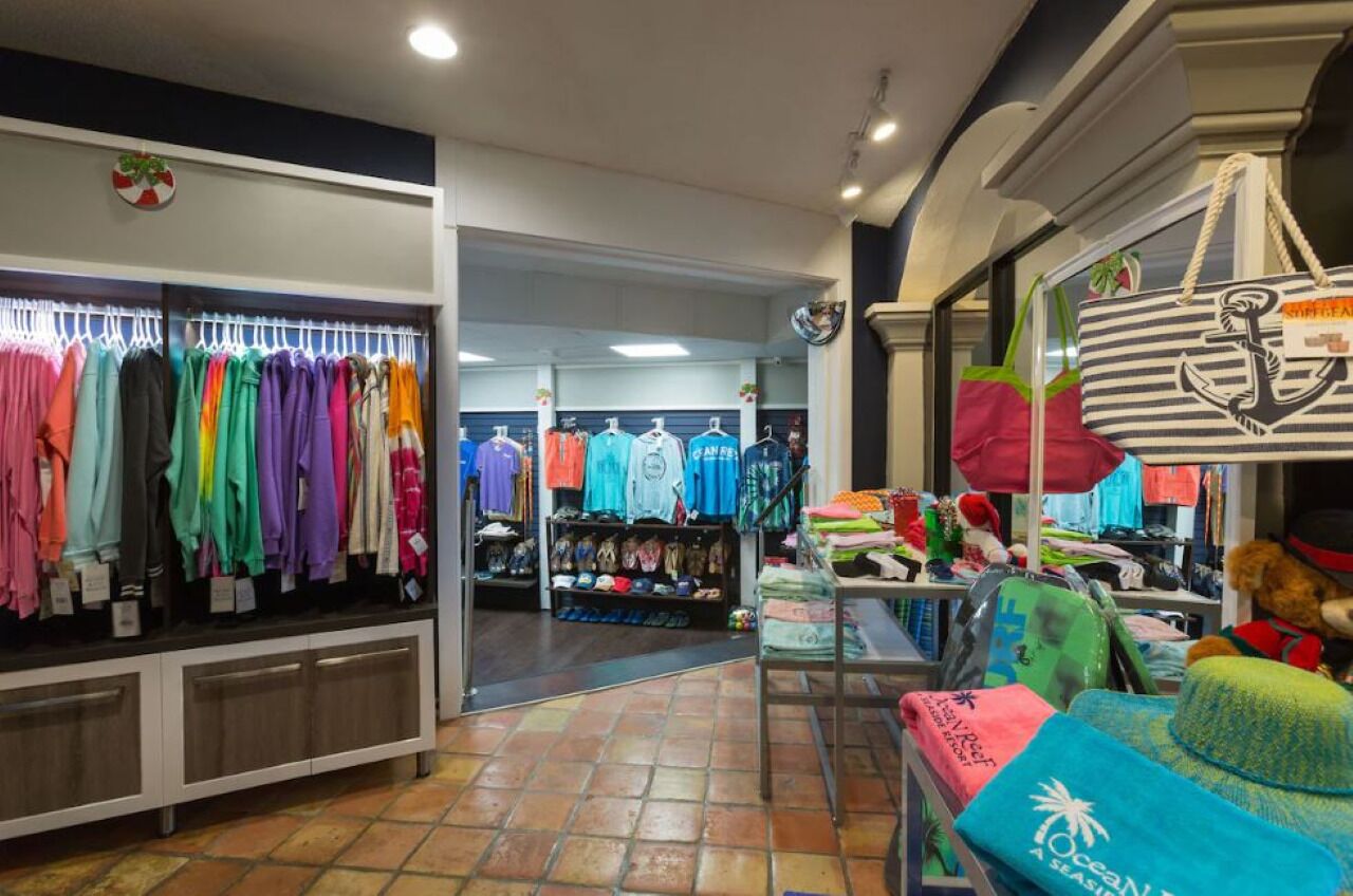A clothing store with racks of colorful shirts and a display of beach bags and hats.