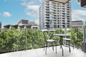 Un balcón con dos sillas y una mesa, con vista a una zona verde exuberante y un edificio alto.