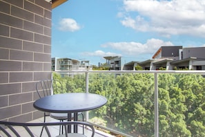 A balcony with a table and chairs, overlooking a residential area with modern buildings and greenery. - Stylish 2 BDR Apt Near QUT And RBWH With Parking (Kelvin Grove)