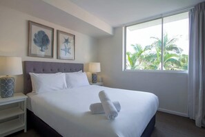 Una habitación de hotel con una cama grande, dos cuadros con forma de estrella de mar, una ventana que da a palmeras y dos lámparas de noche.