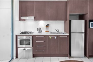 A modern kitchen with stainless steel appliances, wooden cabinets, and a built-in oven. - Stylish 2 BDR Apt Near QUT And RBWH With Parking (Kelvin Grove)