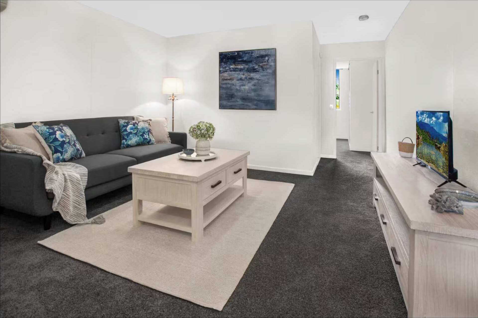 A modern living room with a sofa, coffee table, lamp, and artwork on the wall.