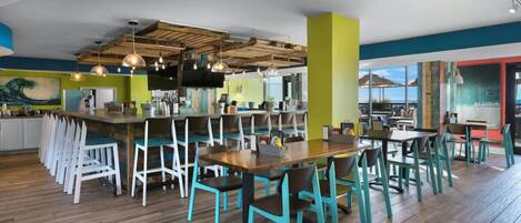 A modern restaurant with wooden floors, teal chairs, and a bar area.
