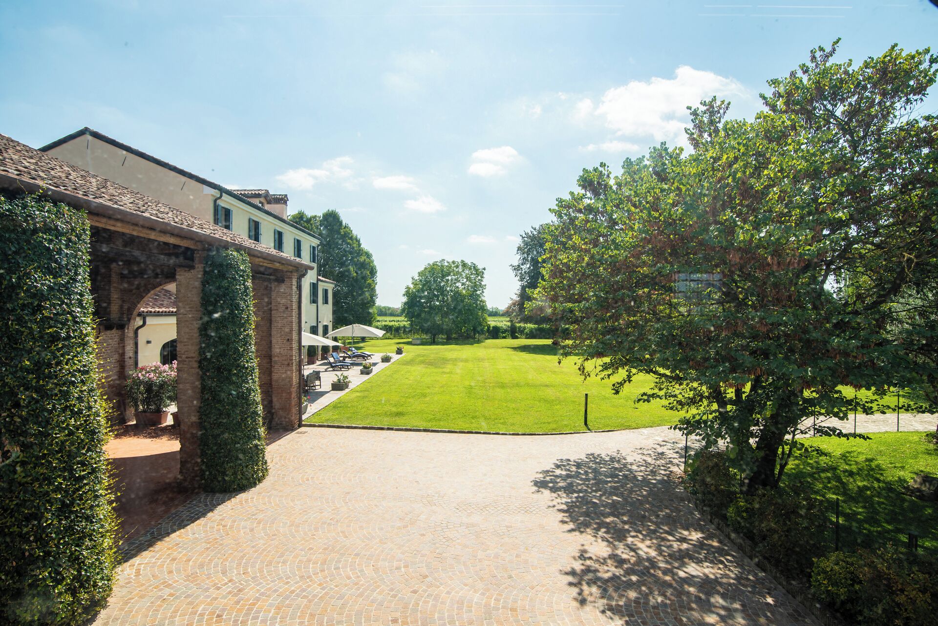 A paved pathway leading to a building with a garden and lawn area.